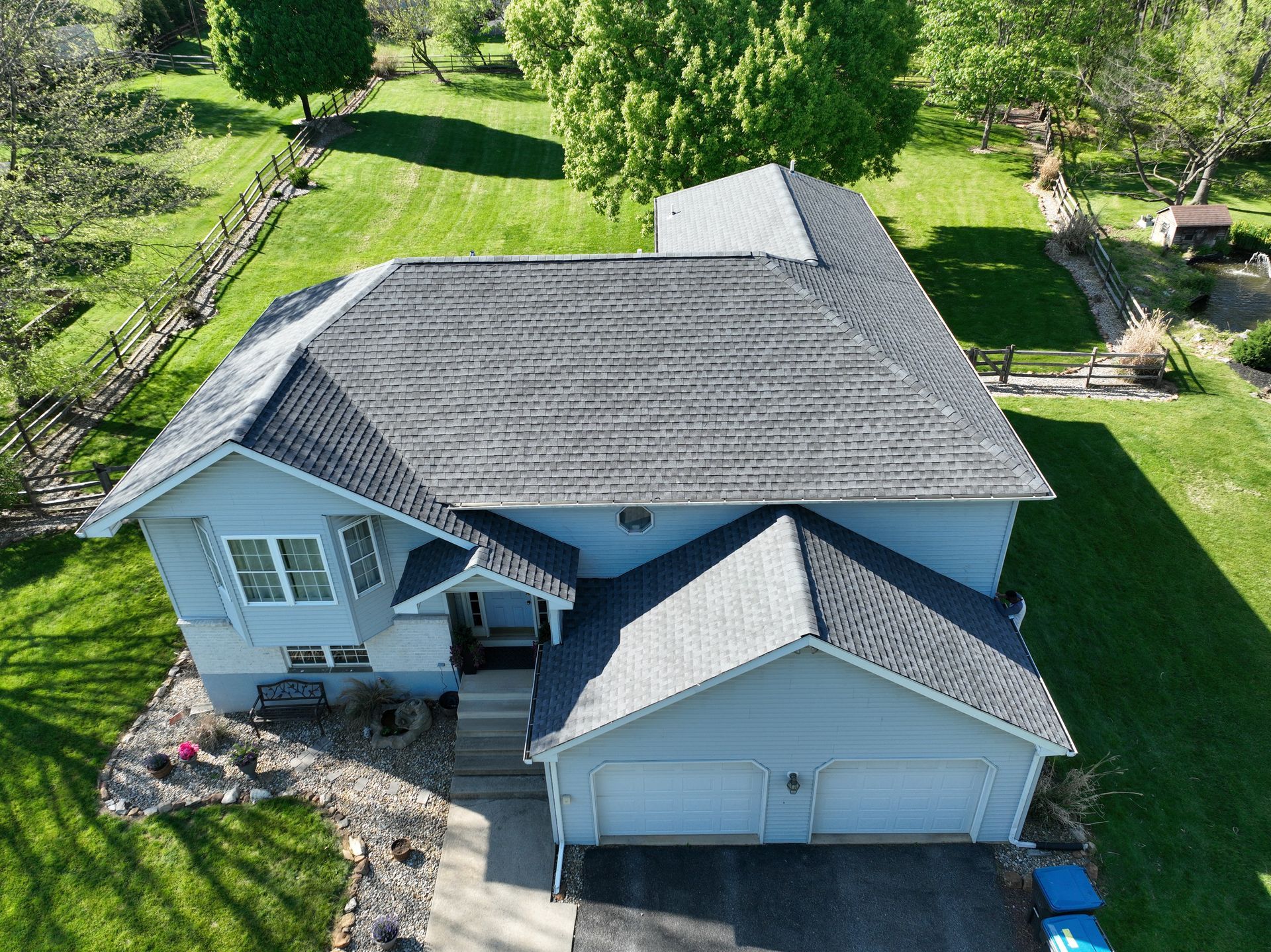 Aerial view of a light blue house with gray roof, front garage, and green yard