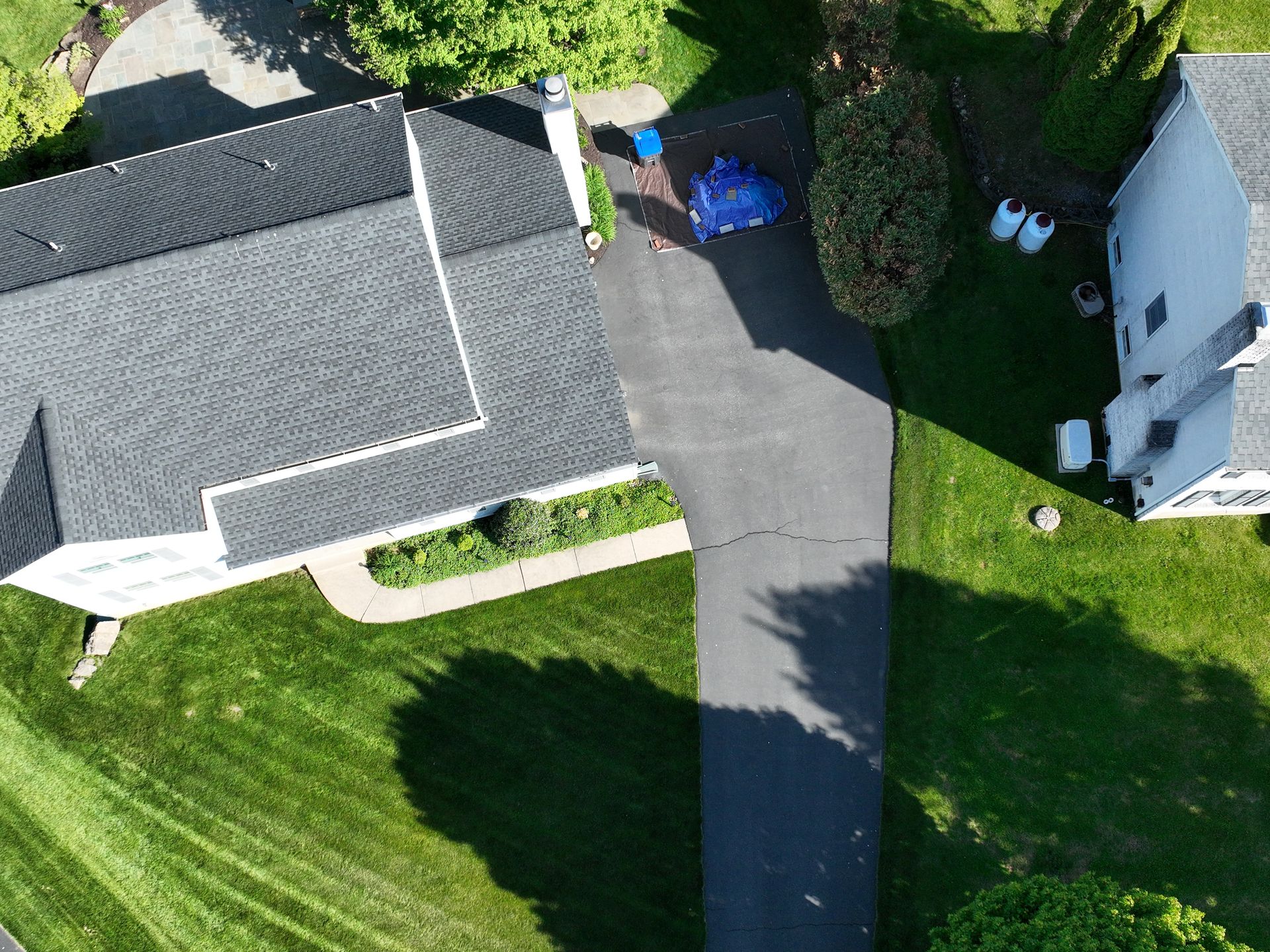 Aerial view of a suburban house with a gray roof, driveway, green lawn, and a parked blue car