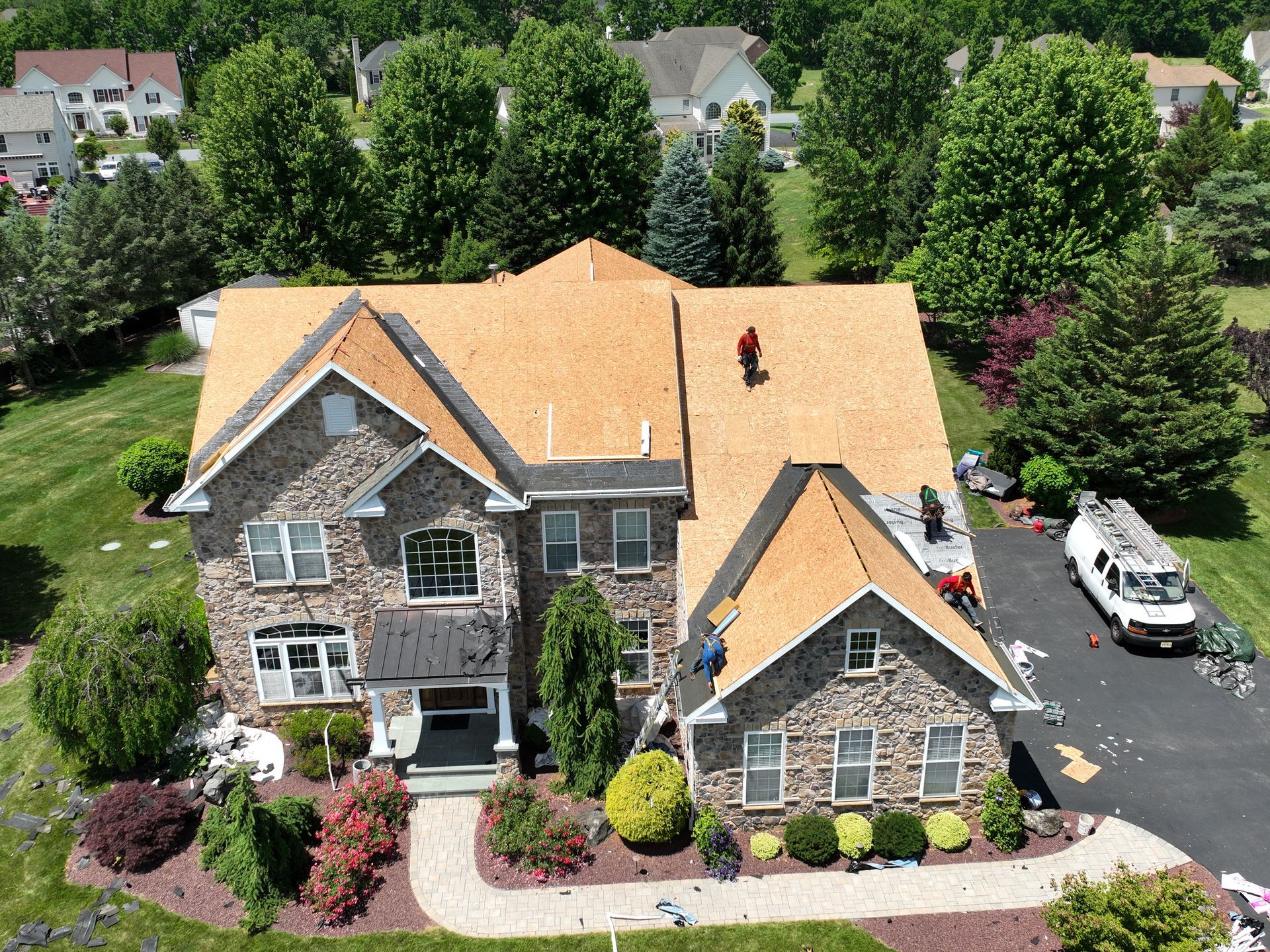 Aerial view of a stone house with an orange roof, landscaped yard, and driveway in a suburban neighborhood
