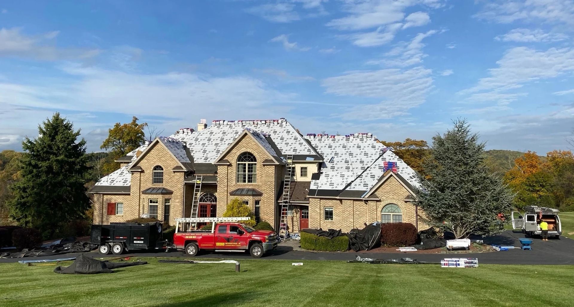 Large stone house with snow on the roof, a red truck parked outside, and trees under a blue sky.