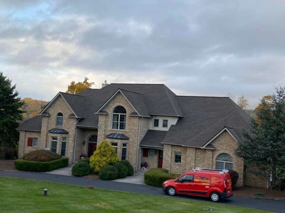 Large stone suburban house with a red SUV parked in the driveway under a cloudy sky