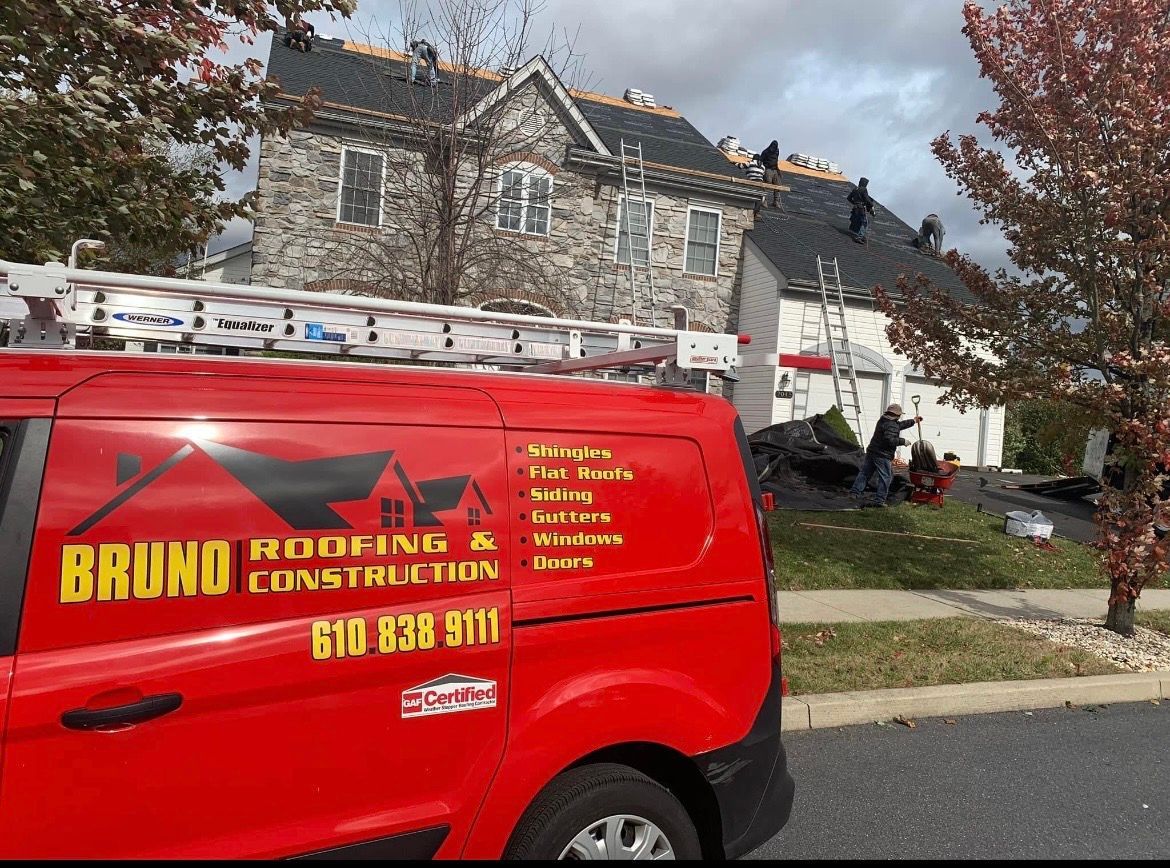 Red HVAC contractor van parked by a stone house with a ladder on the roof and workers nearby