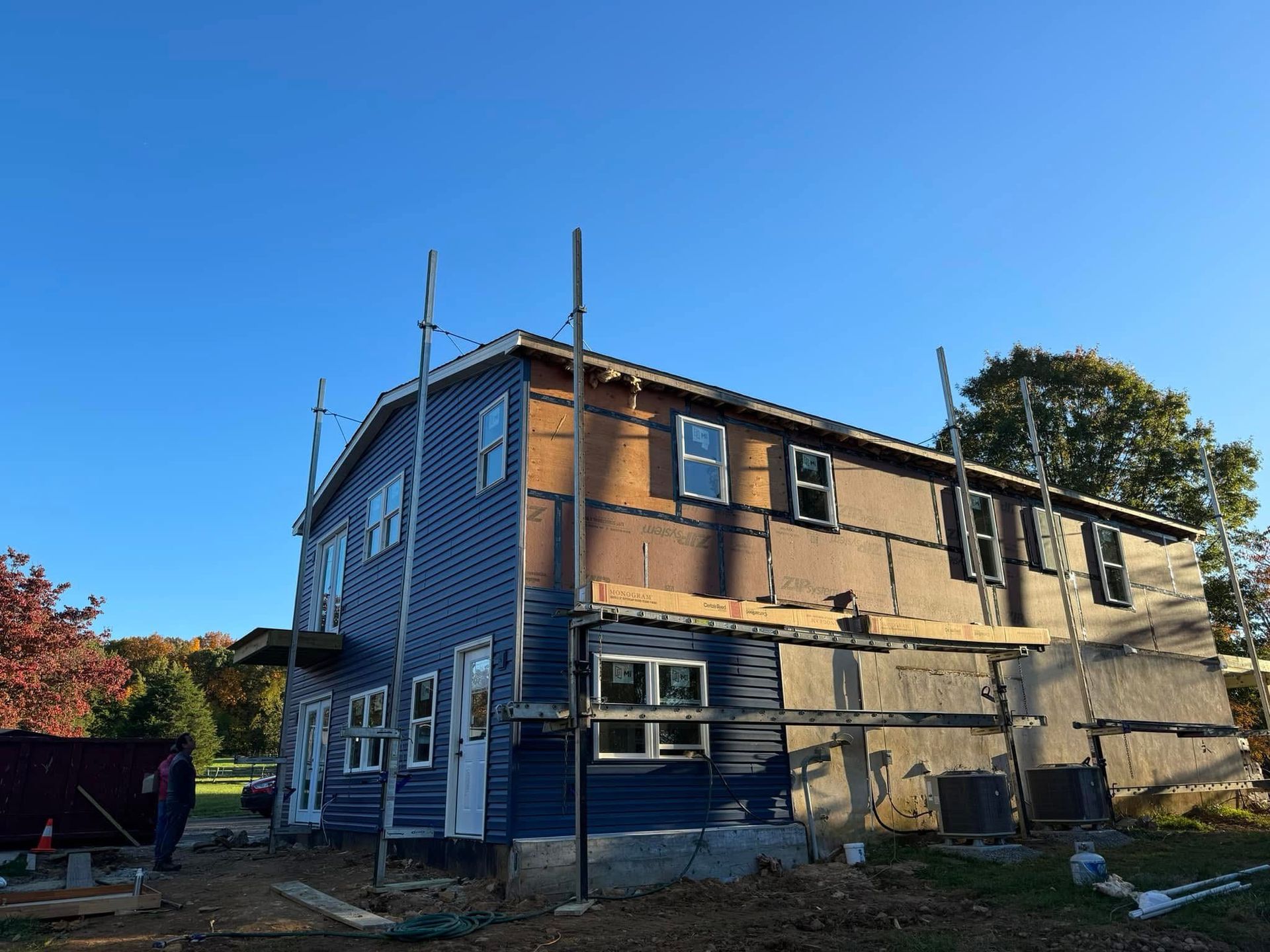 Two-story house under renovation with scaffolding and exposed insulation in bright sunlight
