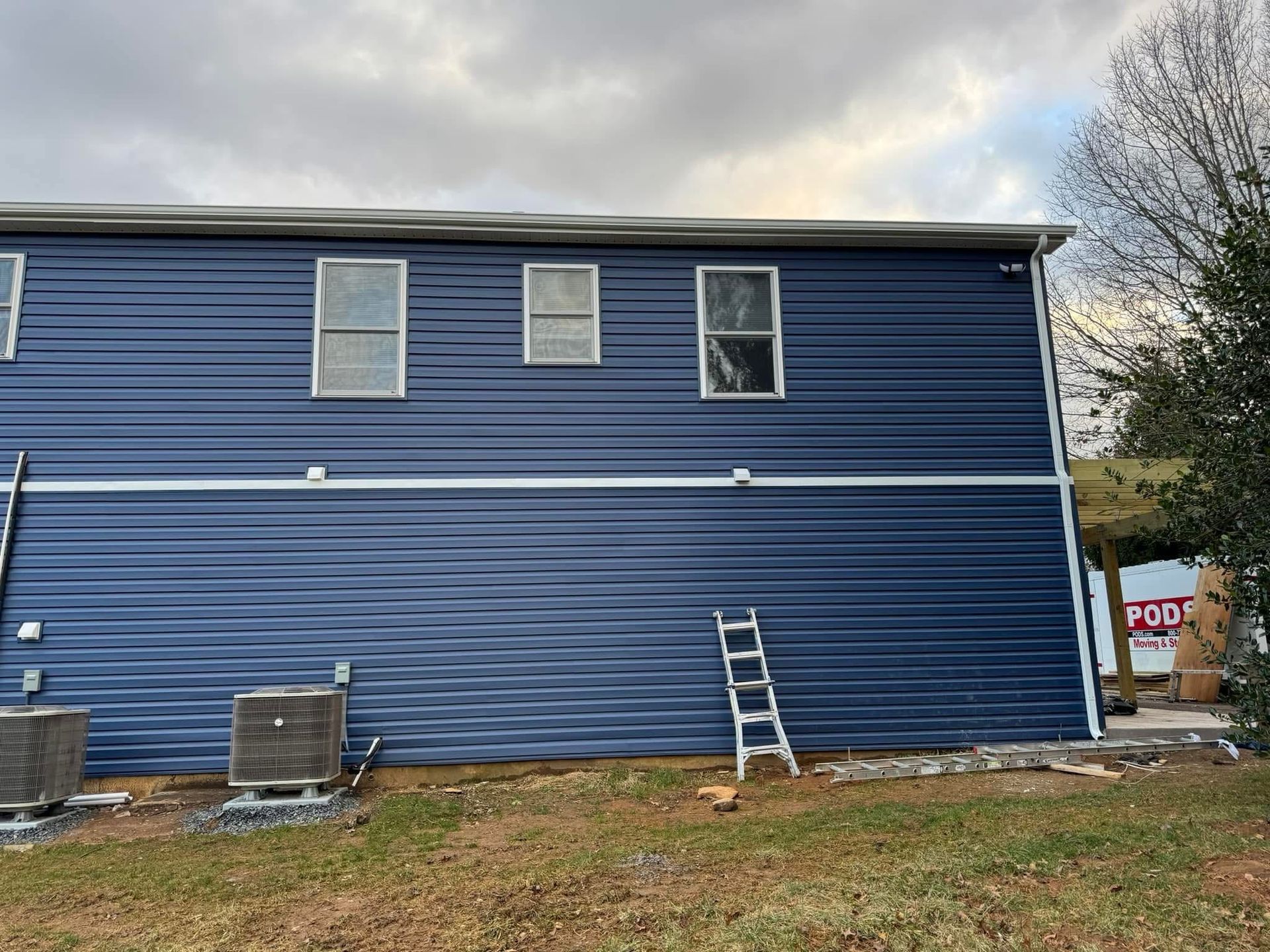 Blue two-story house exterior with ladder leaning against wall and windows above the siding