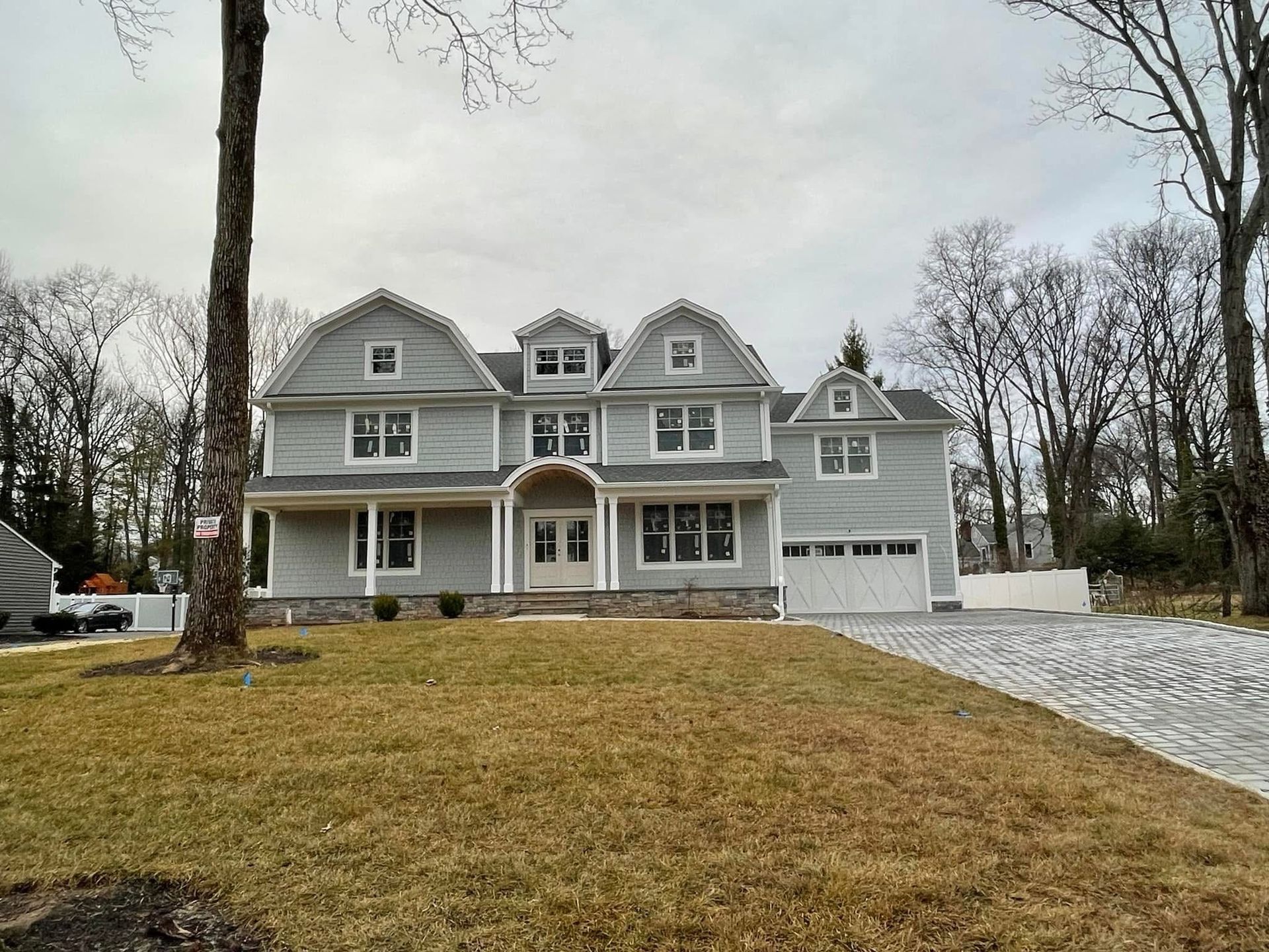 Large gray two-story suburban house with front porch, white trim, and gravel driveway under overcast skies