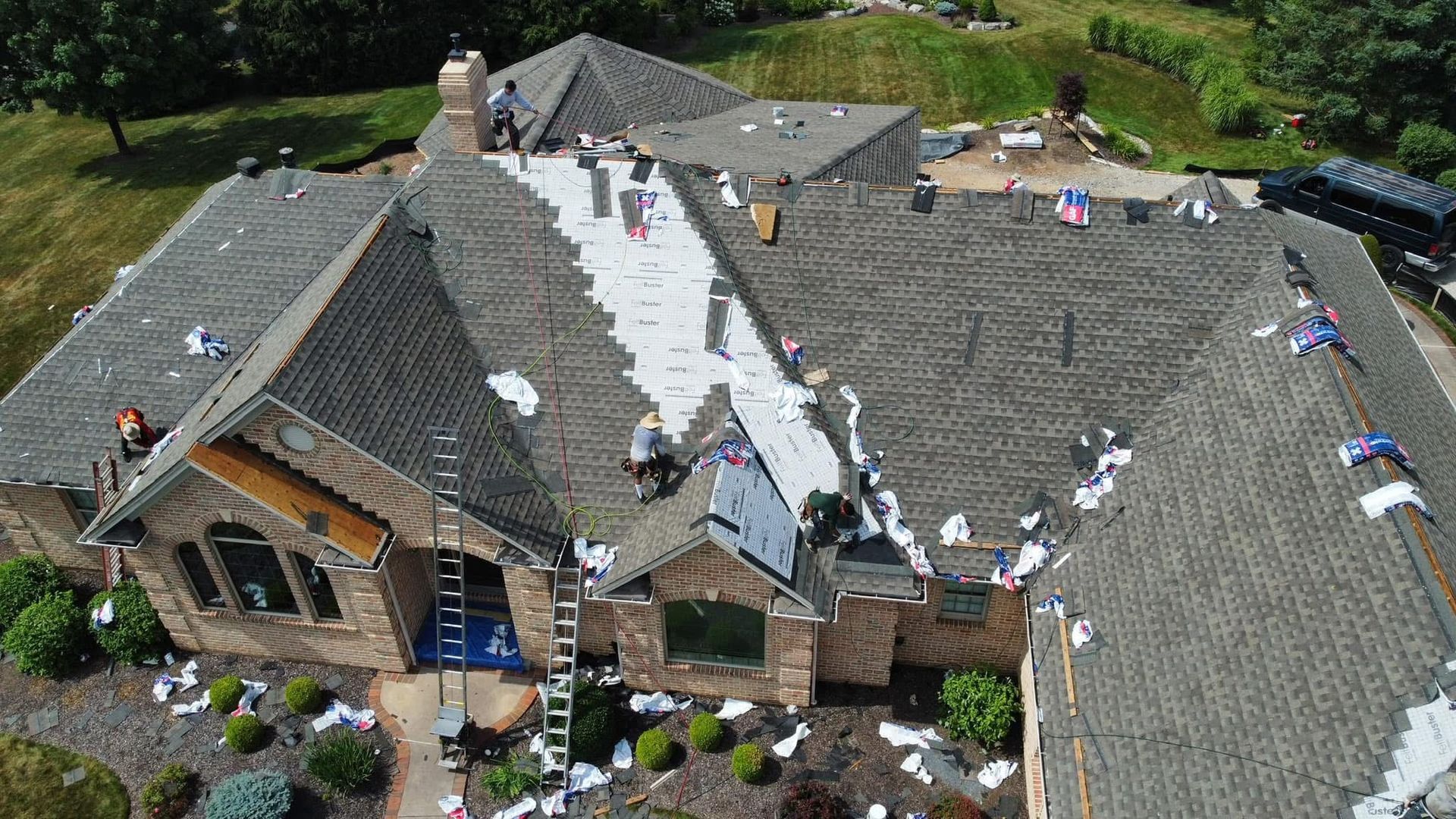 Aerial view of a house with a damaged roof covered by workers during repairs.