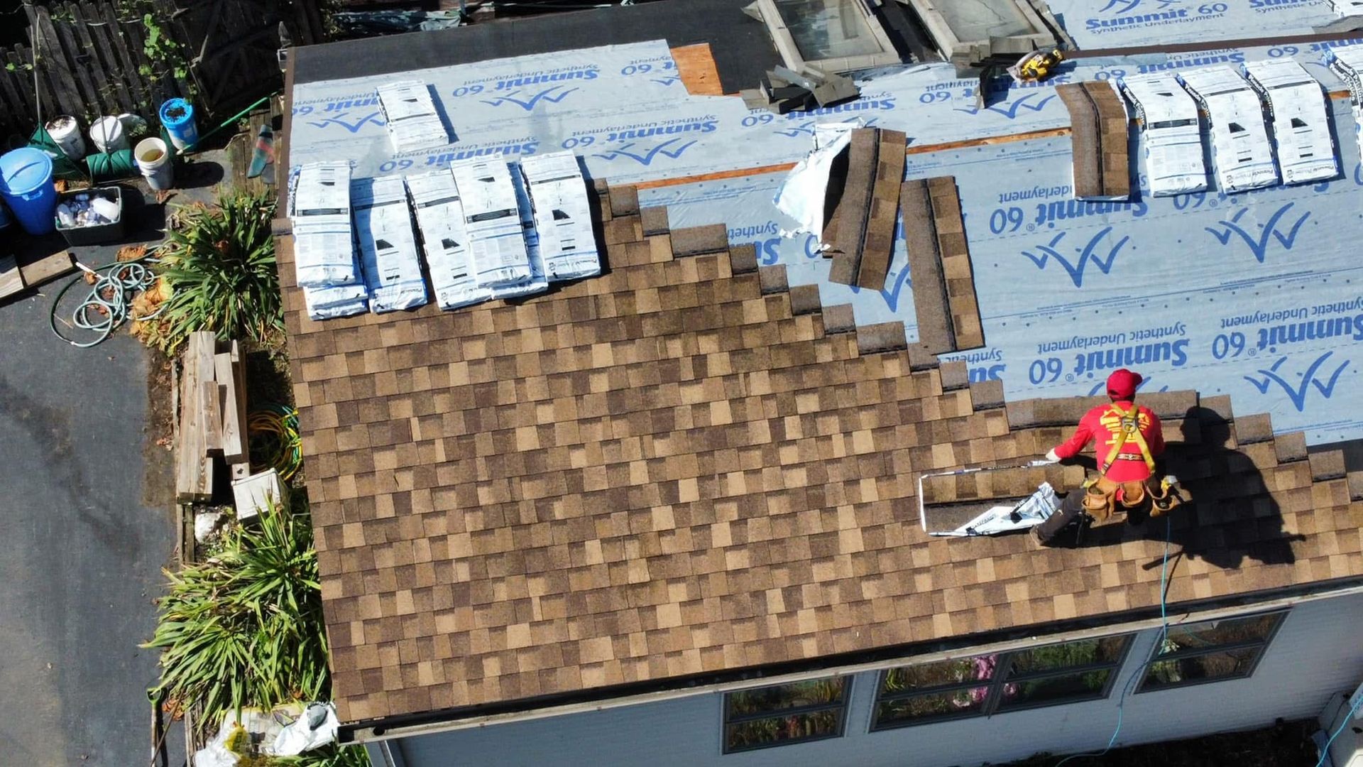 Roofers on a brown shingle roof working near stacked materials and insulation on a building under construction.