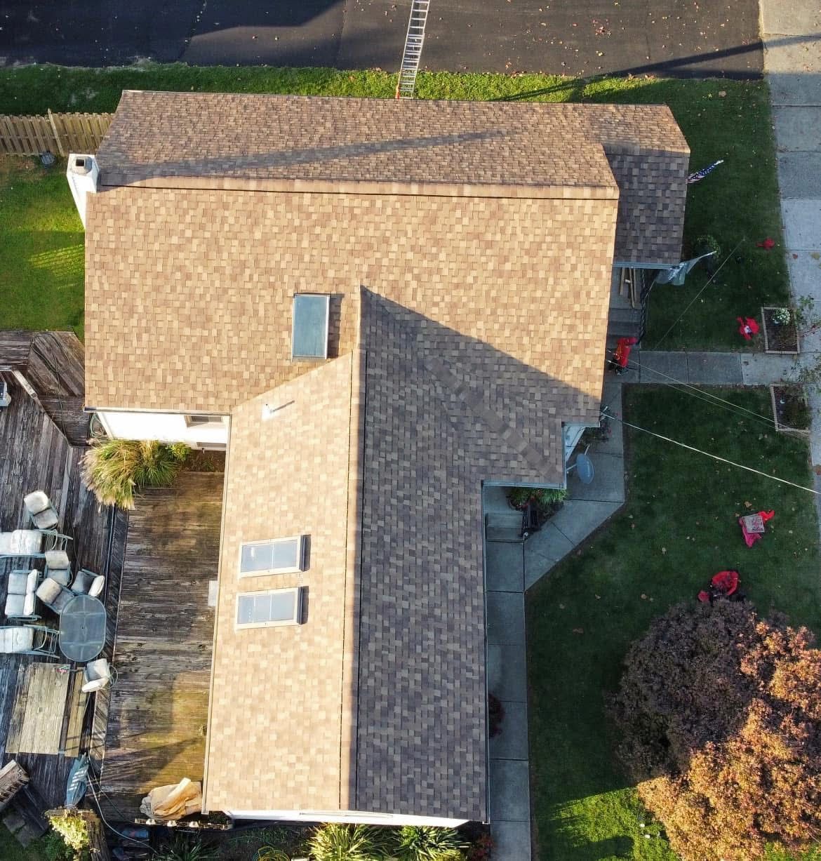 Aerial view of a tan-roofed house with a yard, driveway, and neighboring homes.