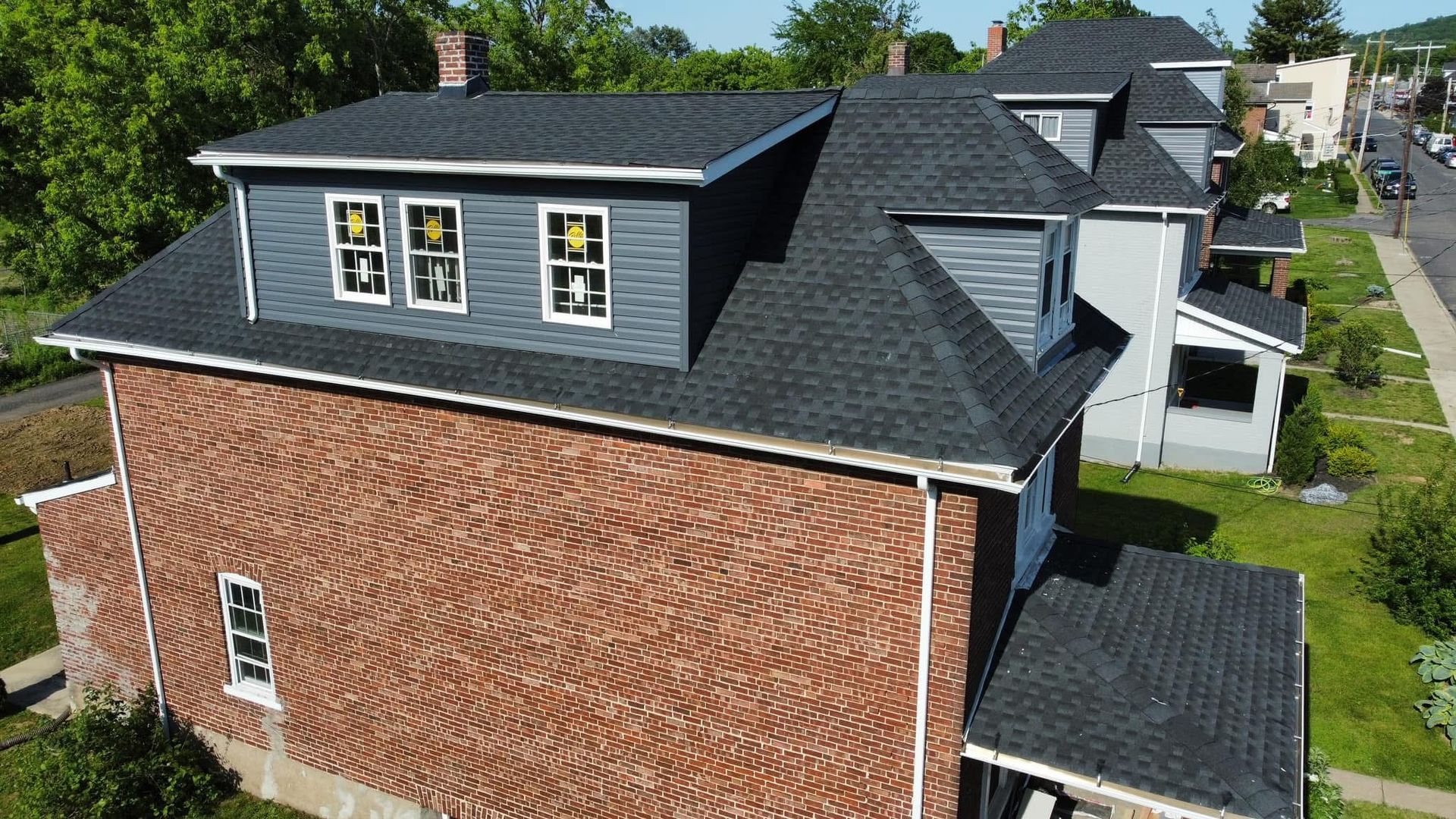 Aerial view of a brick house with a dark roof and dormer windows in a suburban neighborhood