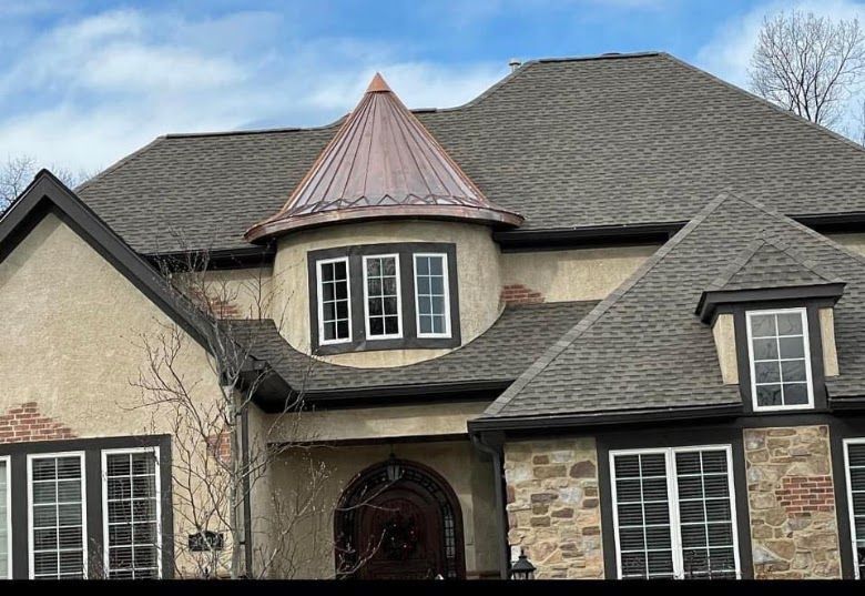 Large stone house with gray shingle roof and copper turret over the front entrance