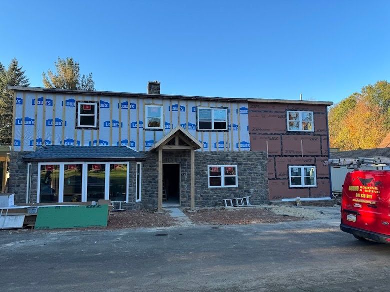 Two-story brick and siding building with windows, parked red van, and autumn trees in front
