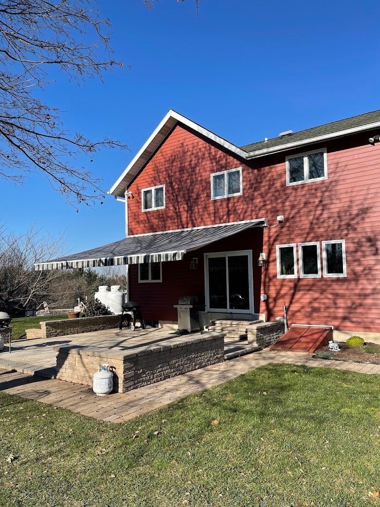 Red two-story house with stone patio and lawn under a clear blue sky
