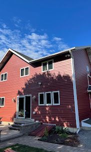 Red two-story house with white trim, front steps, and blue sky overhead