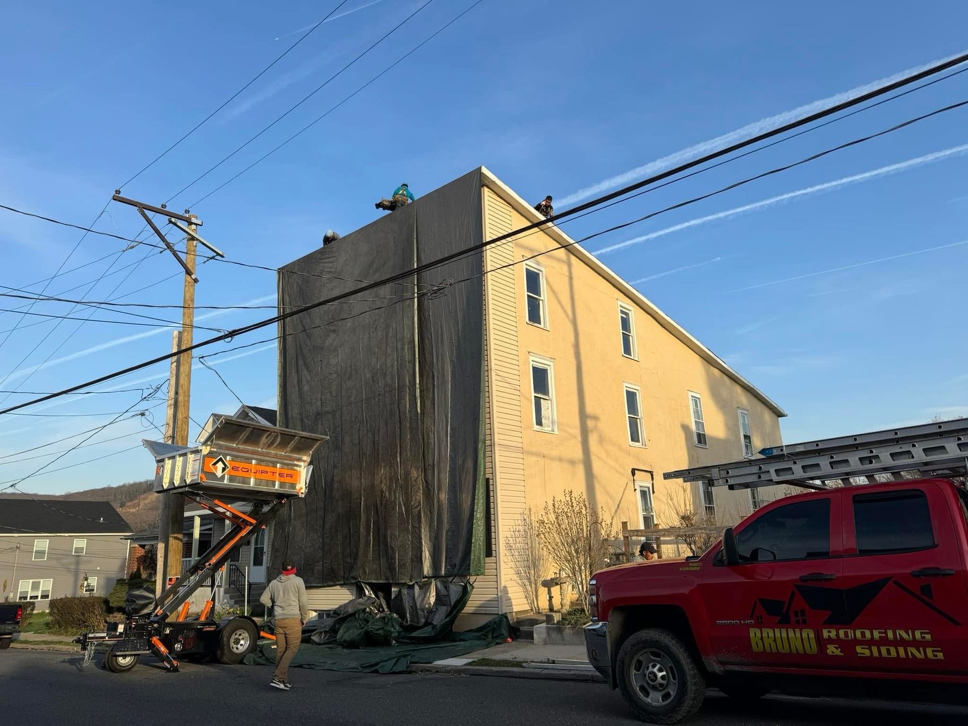 Construction lift beside a tan building, with a red roofing truck in the foreground.