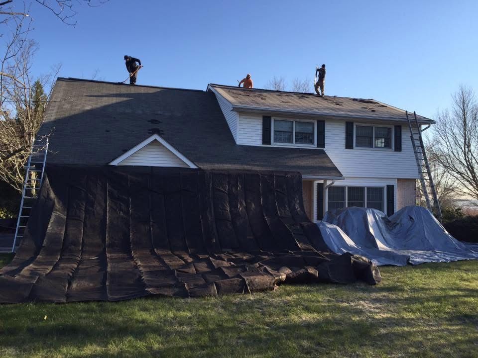 Workers repairing a house roof with tarps covering damaged sections