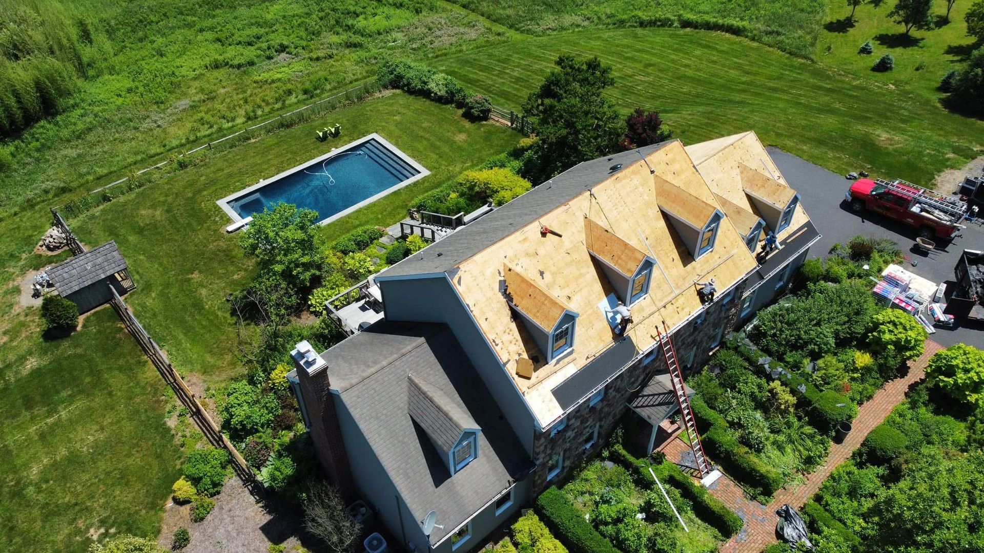 Aerial view of a large house with a swimming pool, green lawn, and parked vehicles.