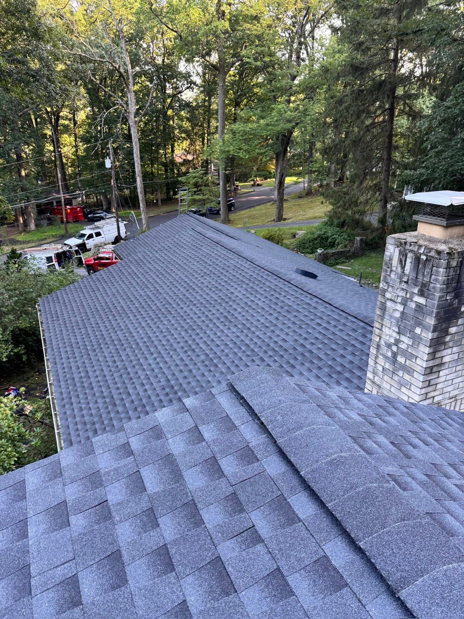 House roof viewed from above amid trees, with a chimney and a glimpse of red patio furniture below