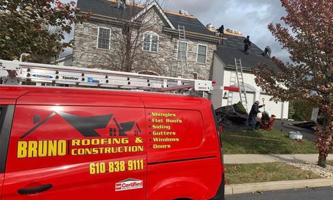 Red Bruno Roofing & Construction van parked beside a stone house on a suburban street.