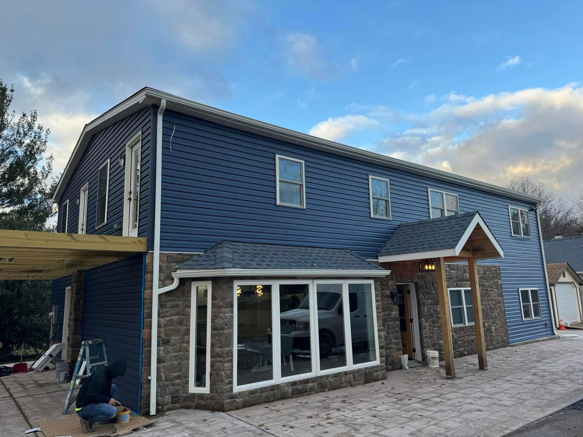 Blue two-story house with stone lower level, large windows, and a covered front entry under cloudy sky