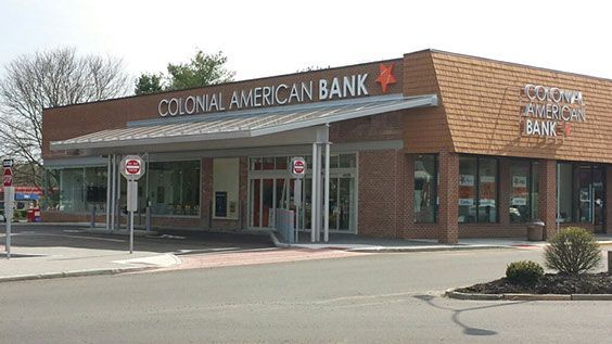 A colonial american bank is located on the corner of a street.