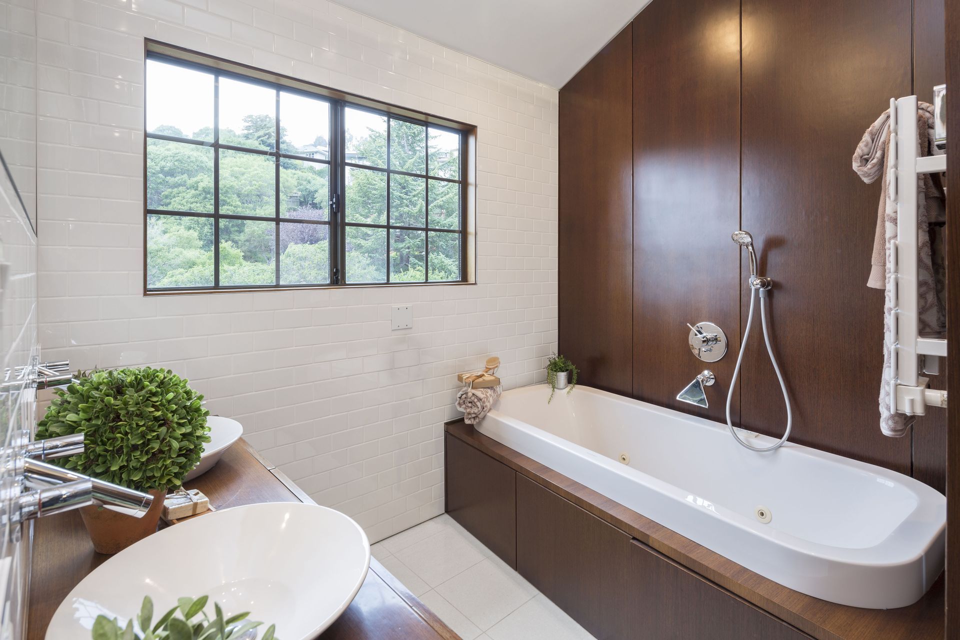Modern bathroom with white tub, dark wood paneling, white sink, and window overlooking trees.