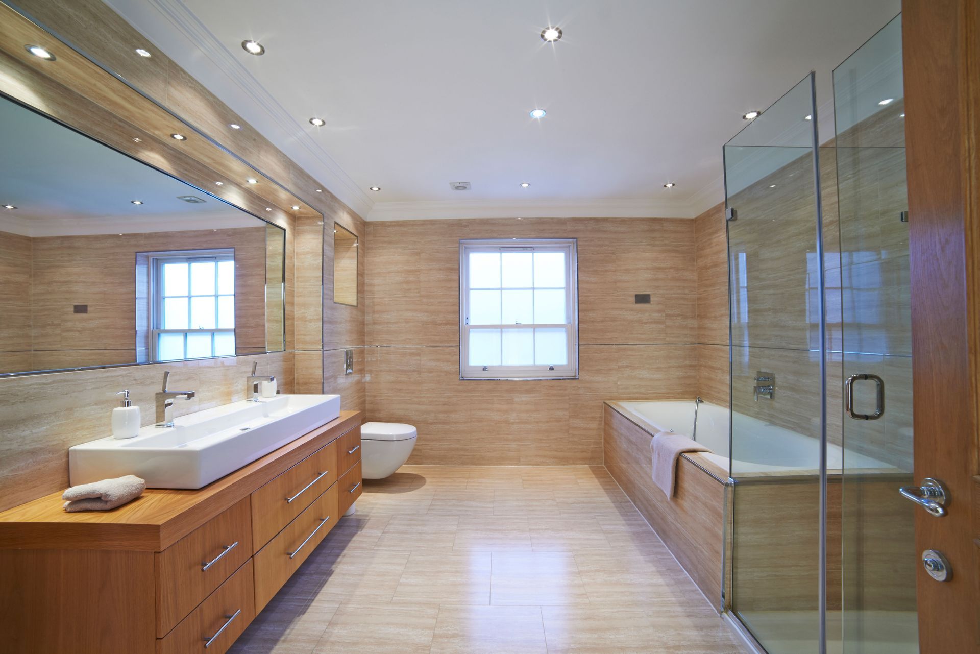 Spacious modern bathroom with a large vanity, tub, and glass shower enclosure. Neutral tones and natural light.