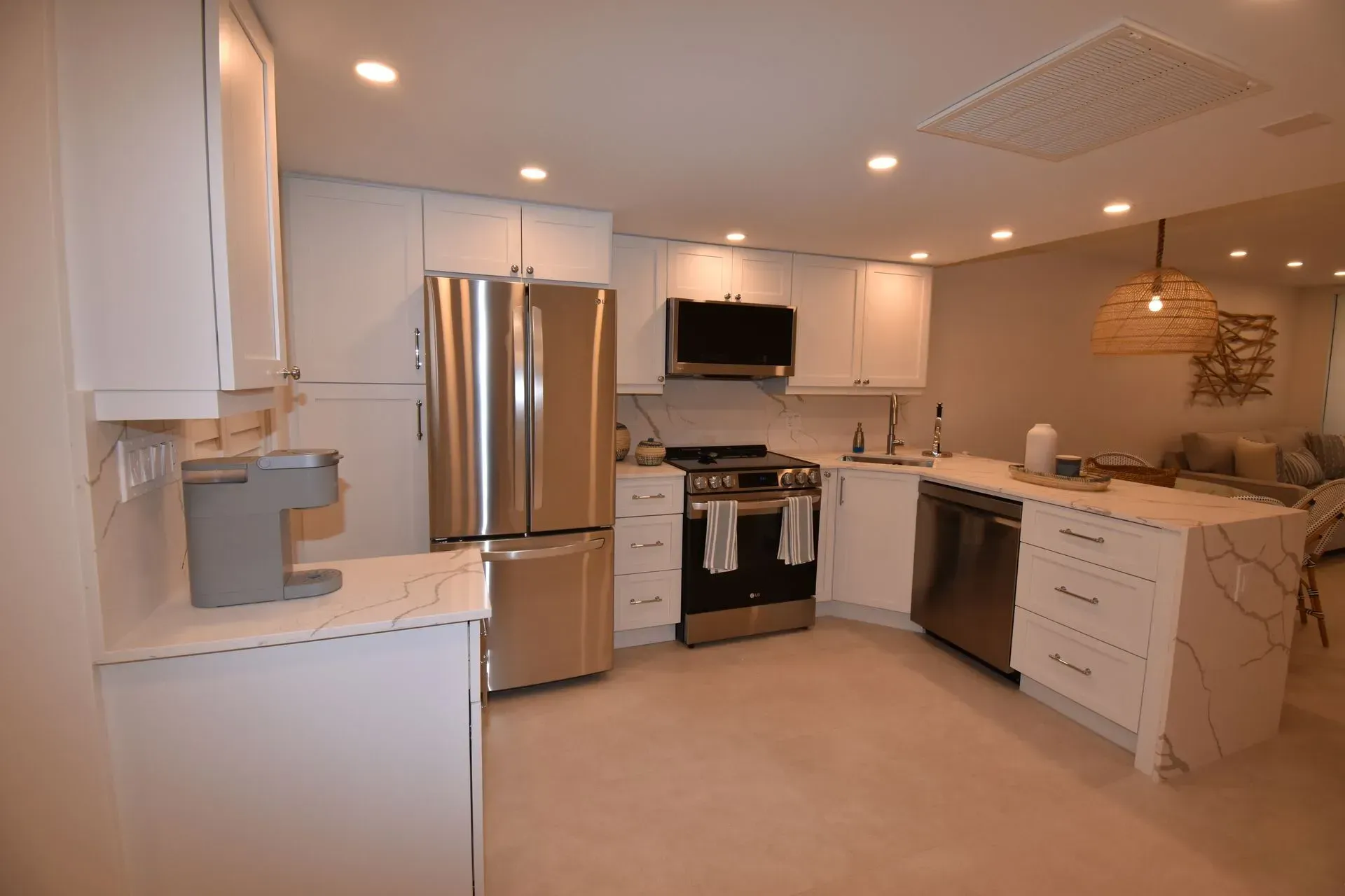 Modern white kitchen with stainless steel appliances, marble countertops, and recessed lighting.