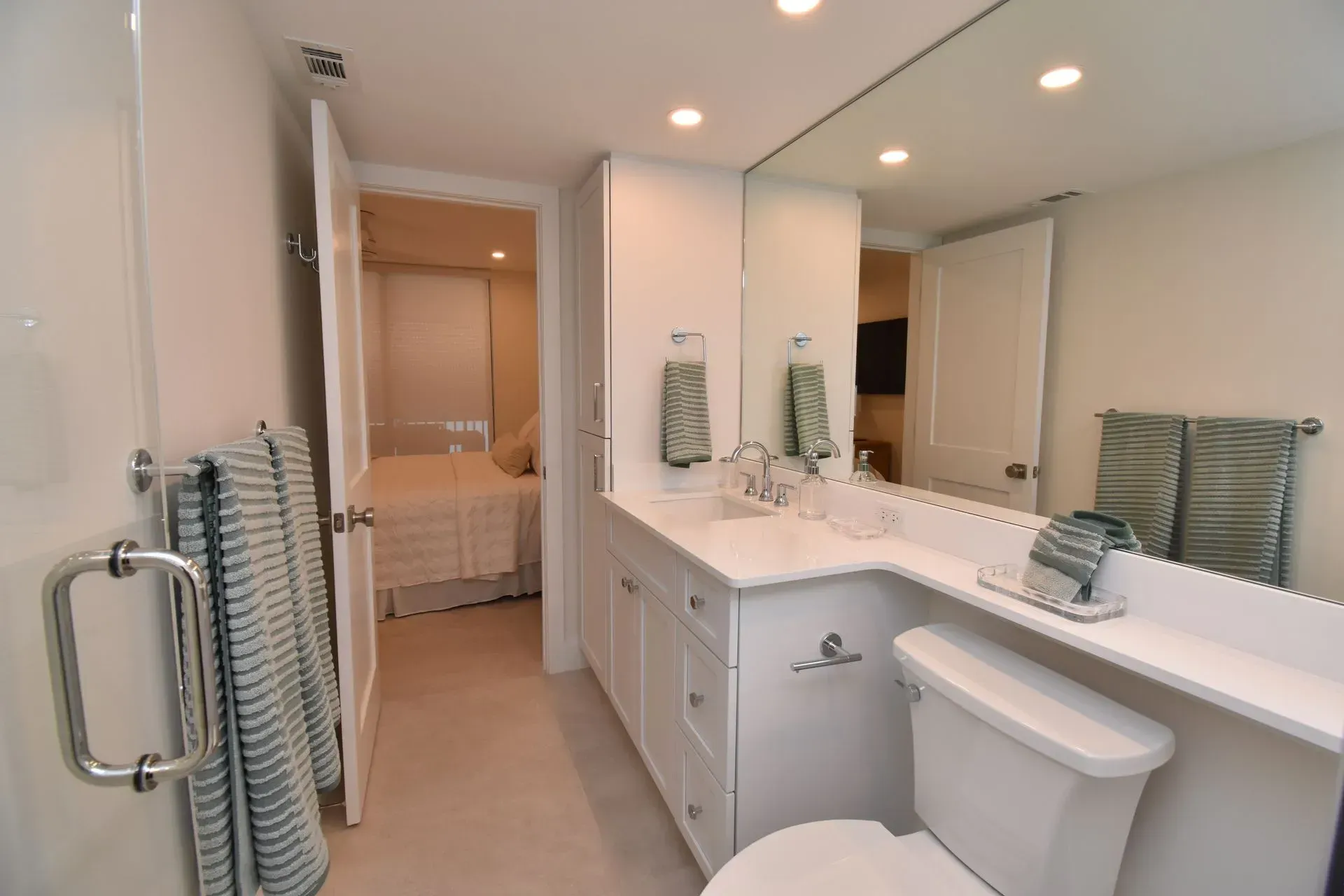 Bathroom with white vanity, toilet, and towels, with bedroom visible through doorway.