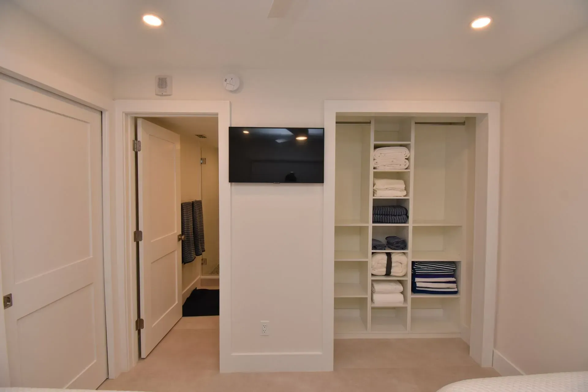 Bedroom with an open closet on the right, bathroom door on the left, TV mounted on the wall.