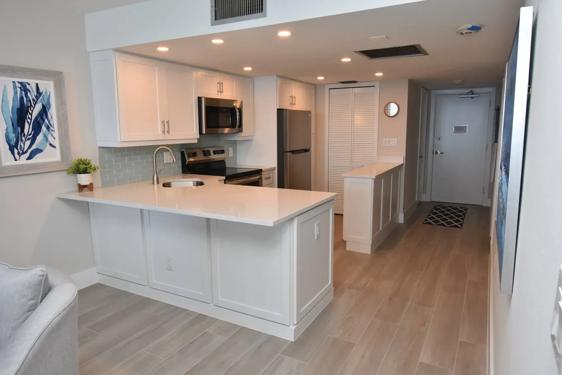 White kitchen with island, stainless steel appliances, and wood flooring.