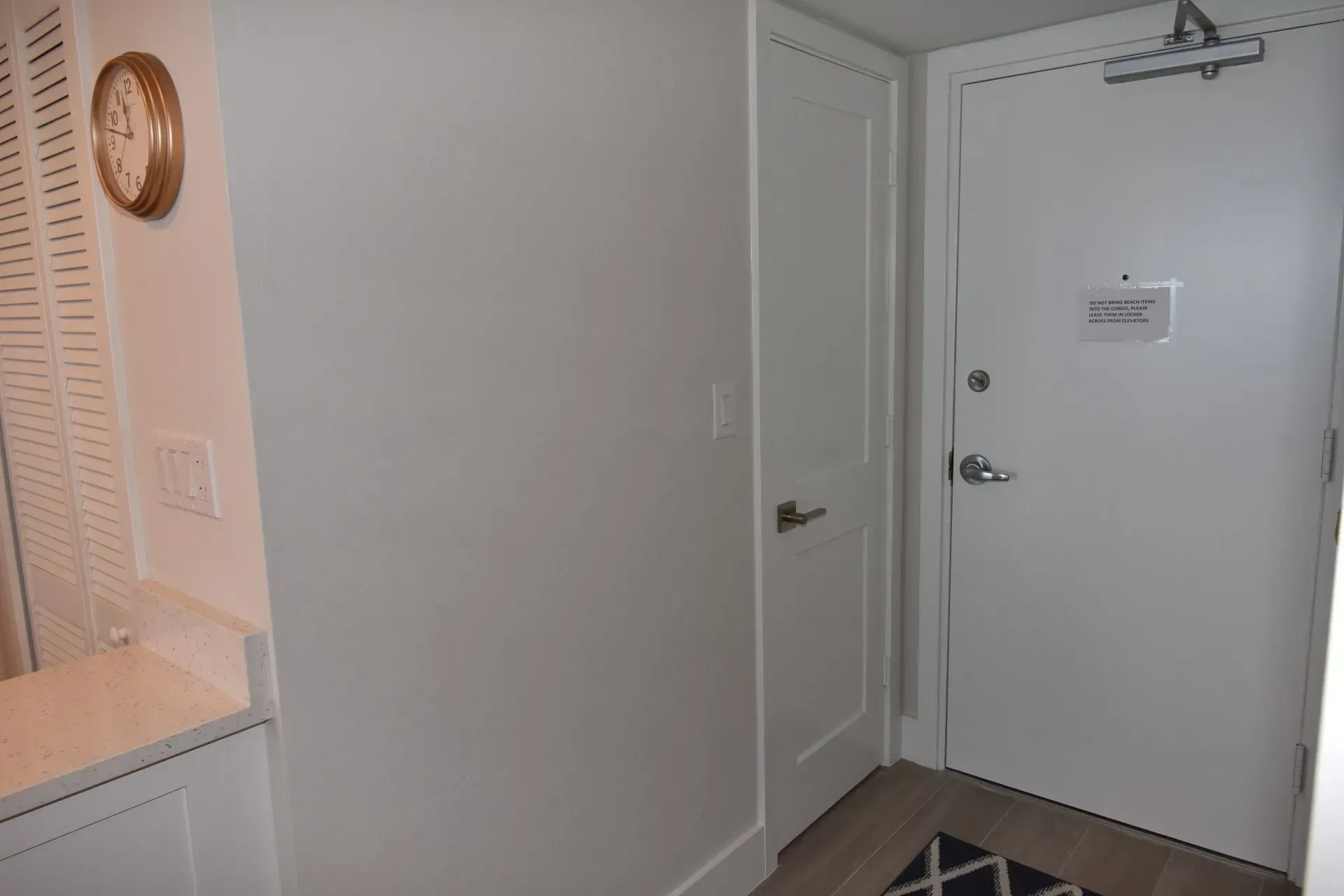 Hallway with white walls, a door, a clock, and a cabinet.