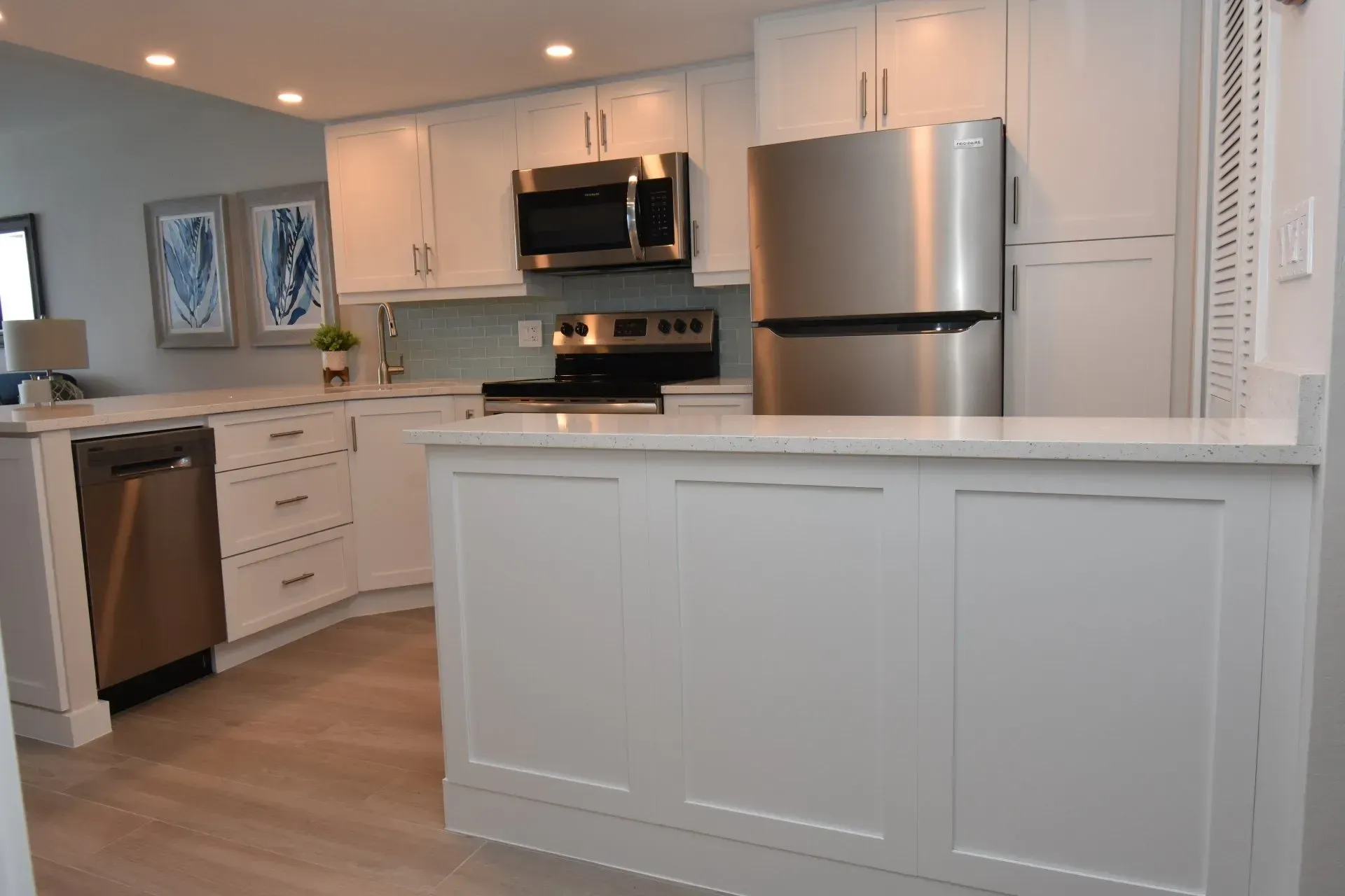 White kitchen with stainless steel appliances, light wood flooring, and framed artwork.