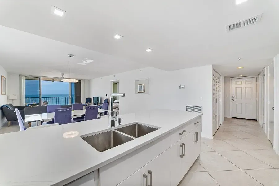 Modern open-concept kitchen with island, stainless steel sink, dining area, and ocean view from a high-rise building.