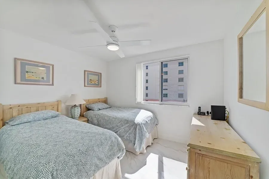 Bedroom with two twin beds, light blue bedspreads, wooden headboards, and a dresser.