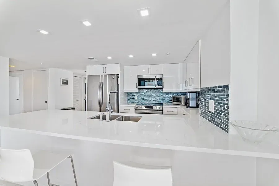 Modern white kitchen with stainless steel appliances, a breakfast bar, and blue-tiled backsplash.