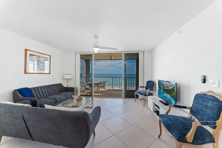 Living room with ocean view, gray sofas, blue chairs, TV, and balcony access.