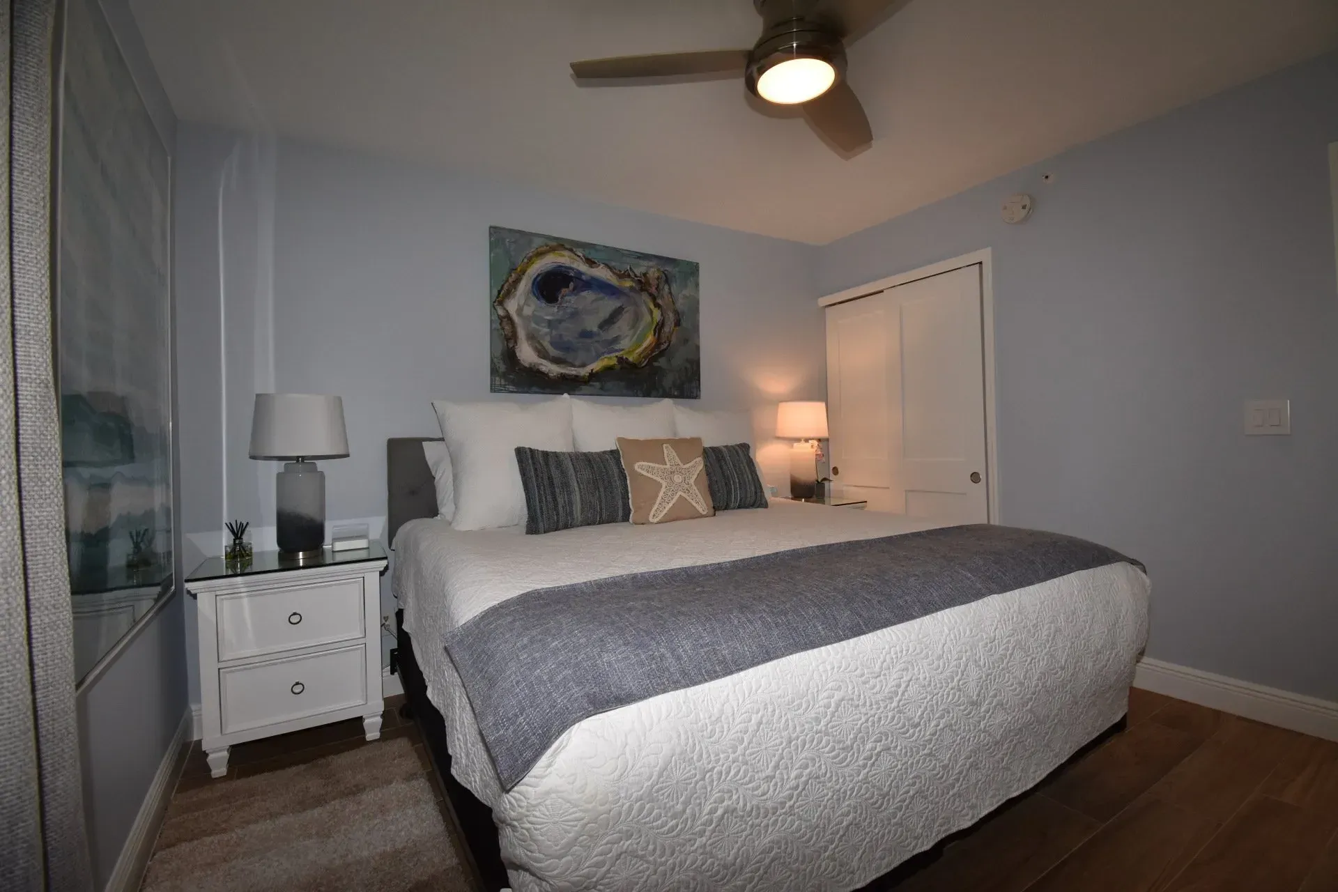 Bedroom with a bed, nightstand, artwork, closet, and ceiling fan; blue and white color scheme.