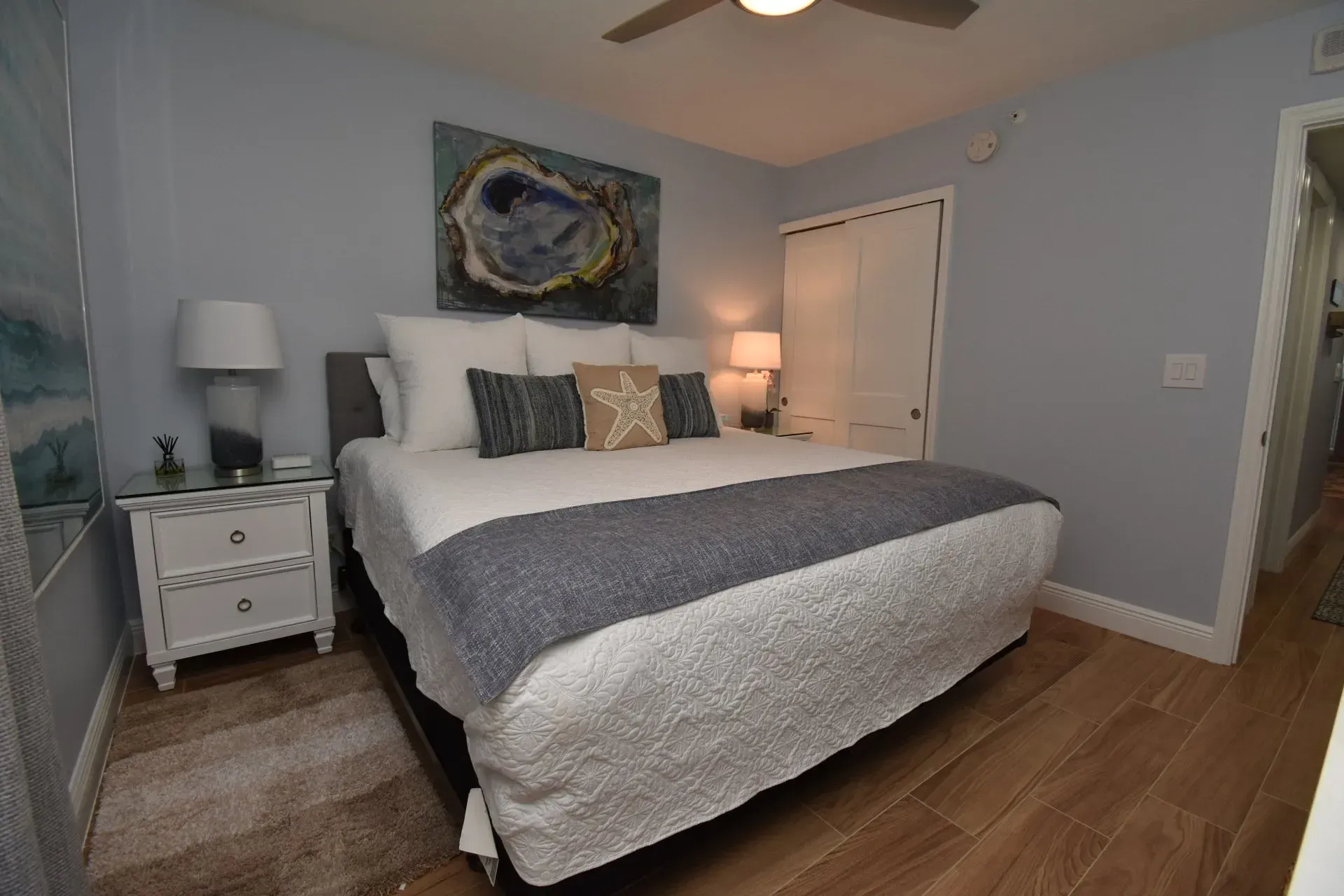 Bedroom with a bed, nightstands, artwork, and a ceiling fan; light blue walls, wooden floors.