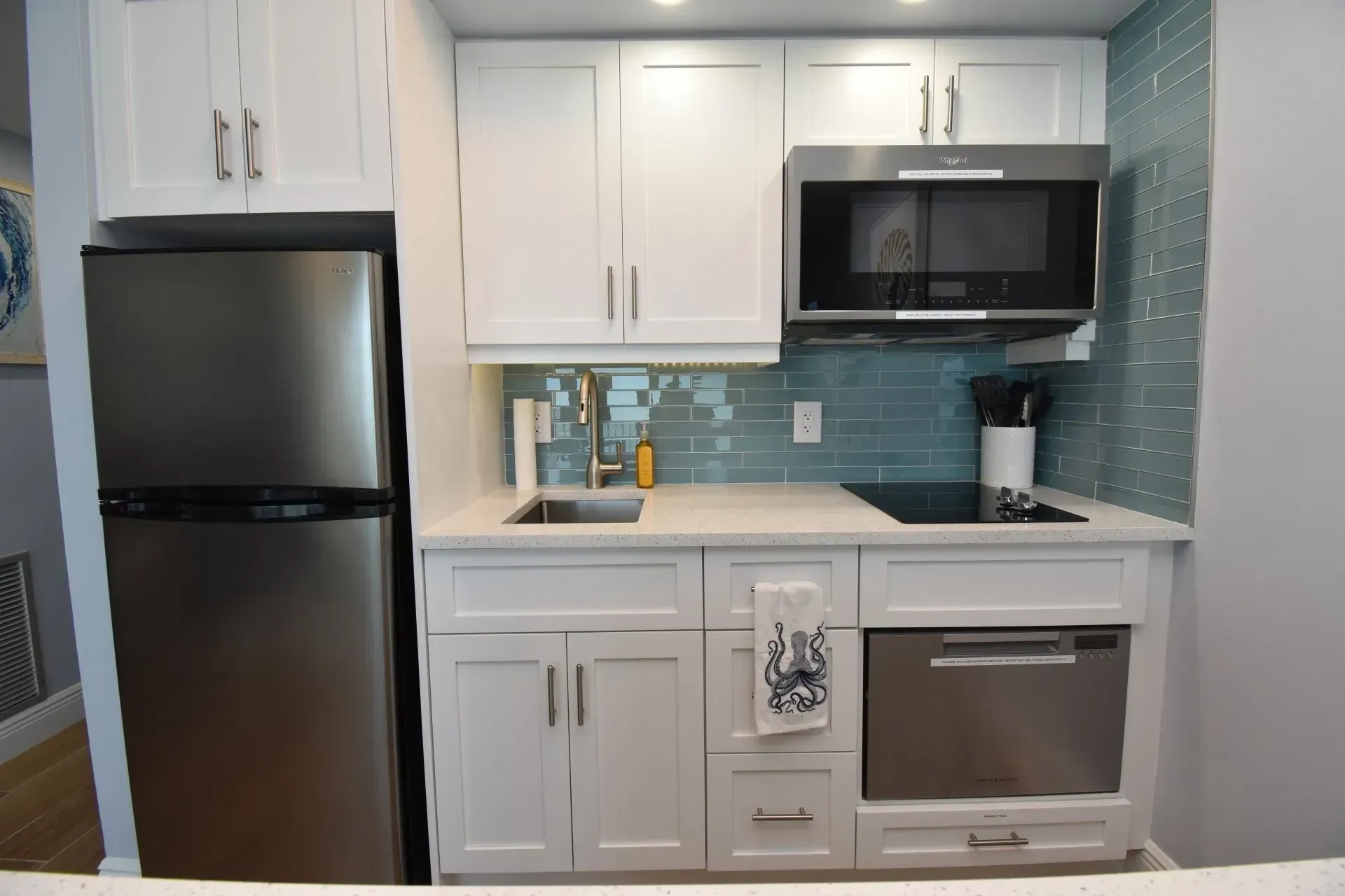 Small, modern kitchen with white cabinets, stainless steel appliances, and blue tiled backsplash.