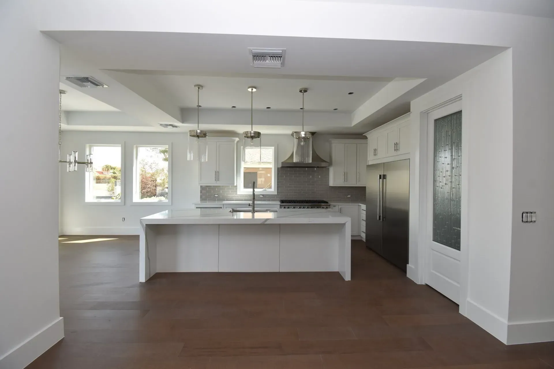 Modern white kitchen with island, stainless steel appliances, and dark wood floors.