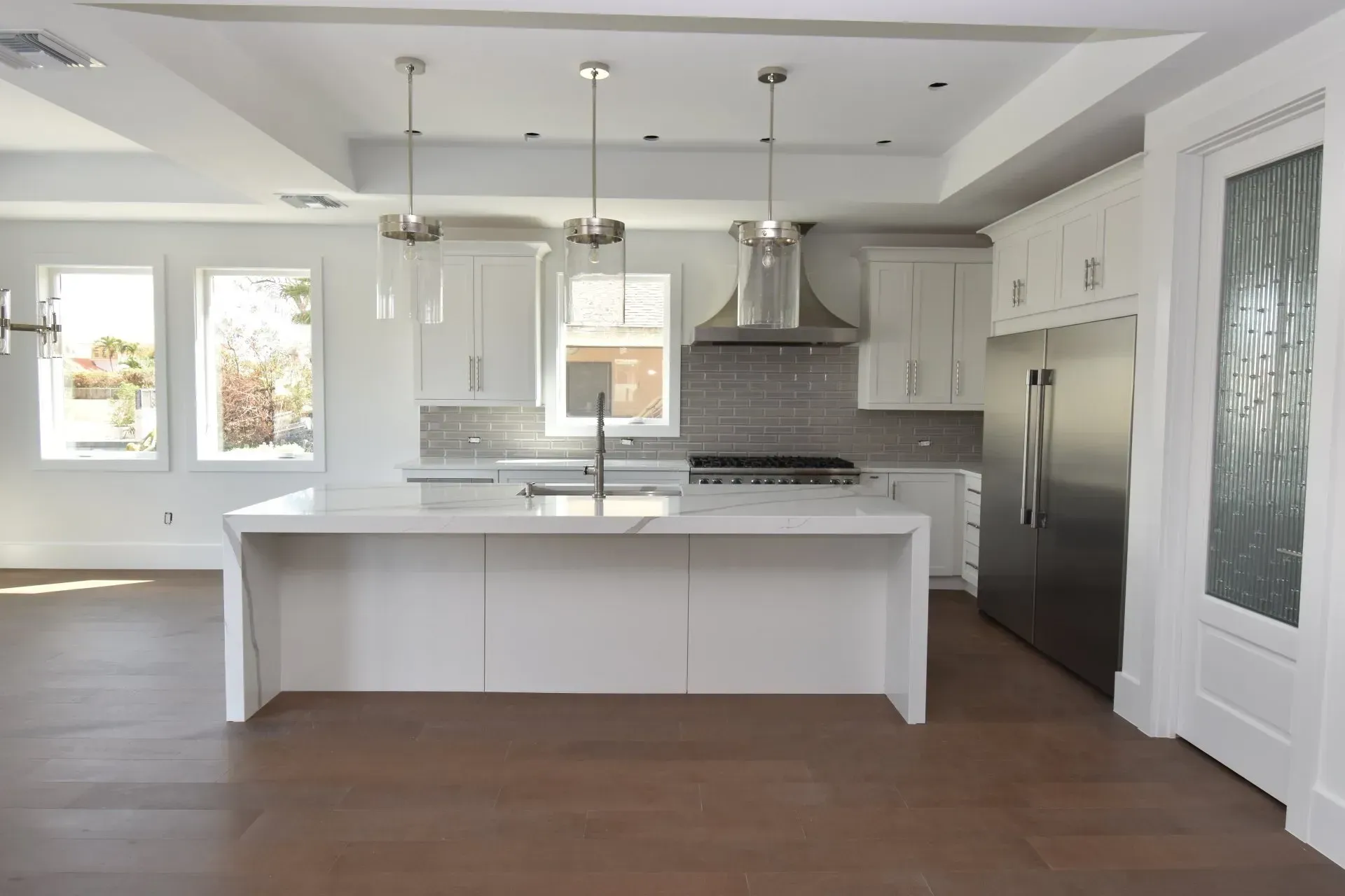 Modern, bright kitchen with white cabinets, island, stainless steel appliances, and dark wood floors.