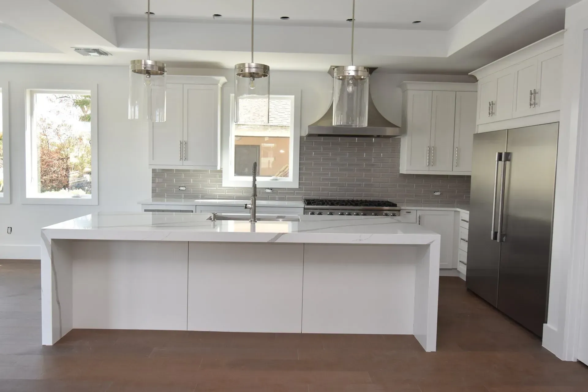 Modern white kitchen with island, stainless steel appliances, and pendant lights.