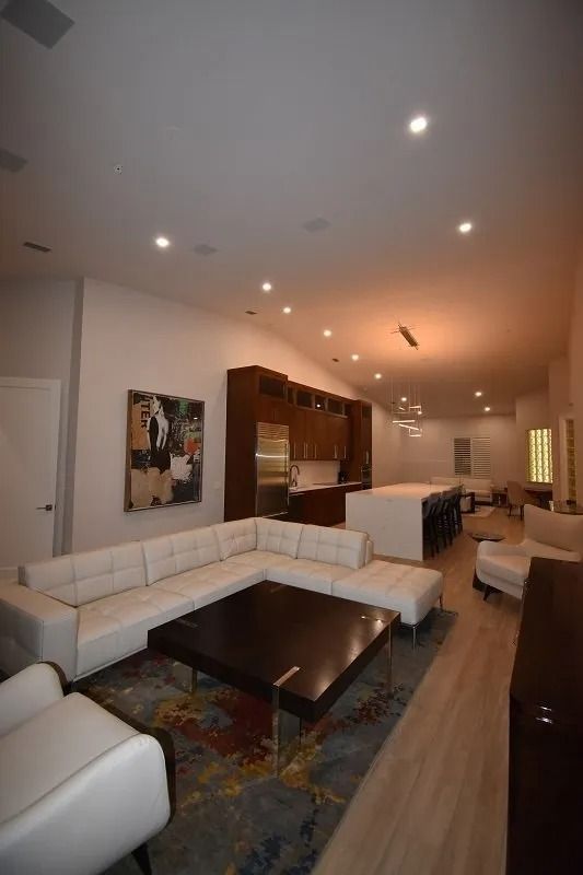 Modern open-plan living space with white sectional, dark wood cabinetry, kitchen island, and recessed lighting.
