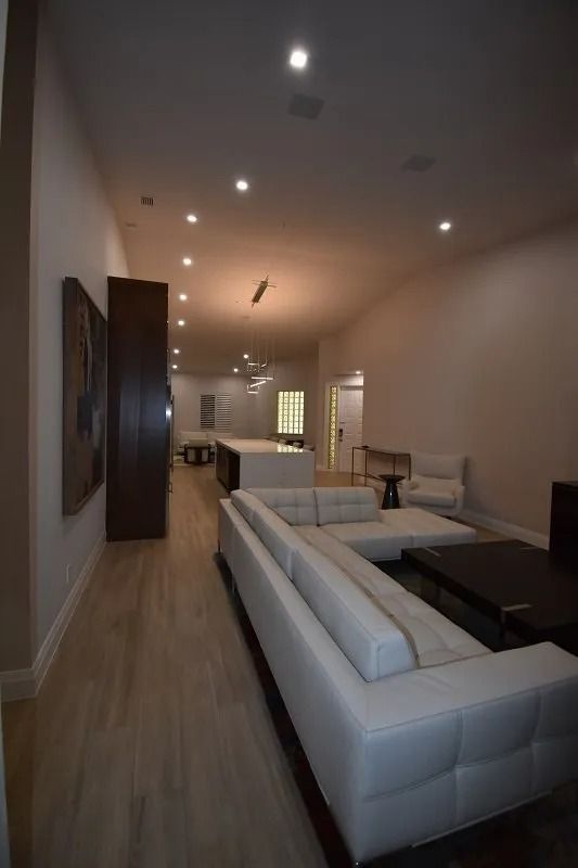 Modern living room with white leather sofa, light wood floors, and recessed lighting.