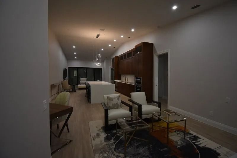 Modern open-concept living area with wood cabinets, white island, light wood floors, and armchairs on a patterned rug.