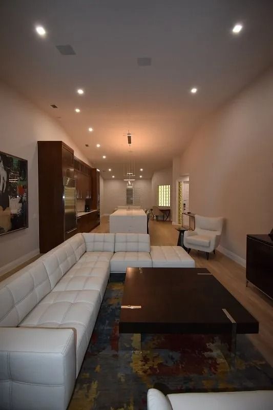 Modern living room with white sectional, dark coffee table, and wood cabinets; light-colored floors and walls.