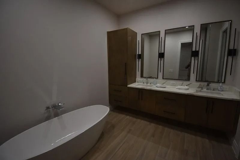 Bathroom with white tub, wood vanity with three mirrors, and a tall cabinet.