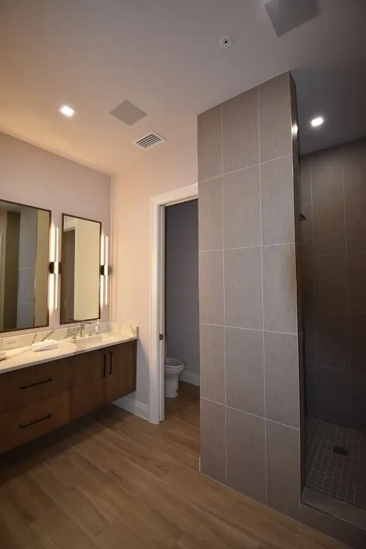 Modern bathroom: floating vanity with mirrors, walk-in shower, neutral tones, wood-look flooring.