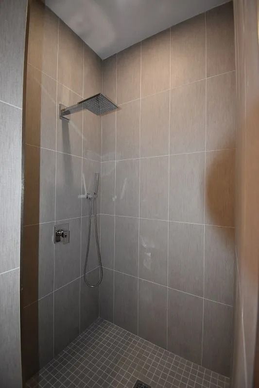 Gray tiled shower with a rainfall showerhead and handheld shower.
