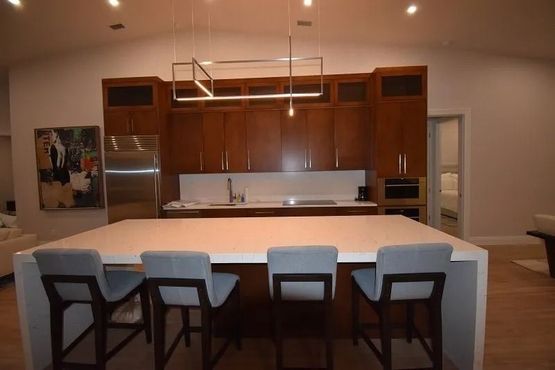 Modern kitchen with large island and bar stools; dark cabinets and stainless steel appliances.